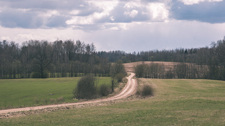Winding country Road with clouds above and gravel surface surrounded by trees - vintage retro lookの写真素材