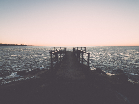 sunset over frozen sea with ice blocks and dramatic colorful sky with old metal bridge - vintage retro grainy film effectの写真素材