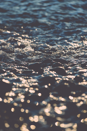 sun reflections on Stones on the beach and sea water in sunset light - retro vintage film effectの写真素材