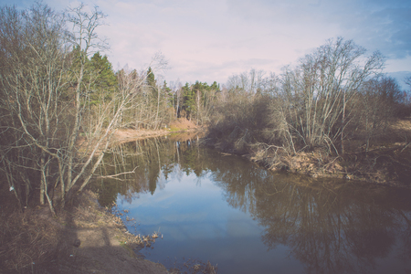 dramatic clouds over the river in misty morning in spring with reflections in water - retro vintage looking effectの写真素材