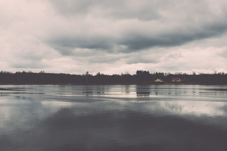 dramatic clouds over the river in misty morning in spring with reflections in water - retro vintage looking effectの写真素材