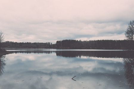 dramatic clouds over the river in misty morning in spring with reflections in water - retro vintage looking effectの写真素材