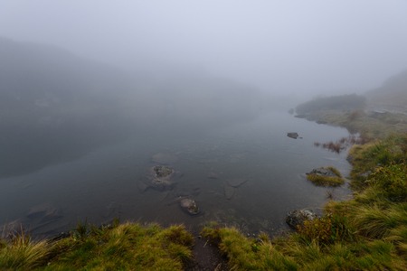 reflections of trees in the lake water at sunrise with morning mist over the water and heavy fog. mountain area water supplyの写真素材