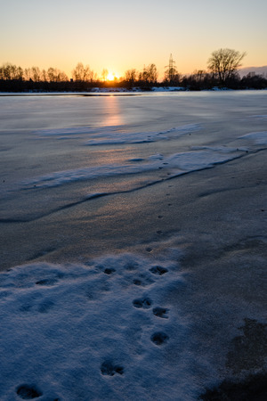 colorful winter sunset on frozen river ice with dramatic cloudsの写真素材