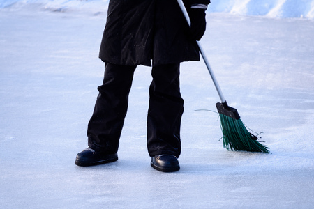 young woman in black coat cleaning ice from snow on a frozen lake to make skating groundの写真素材