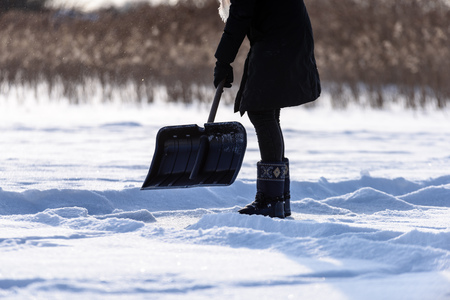 young woman in black coat cleaning ice from snow on a frozen lake to make skating ground