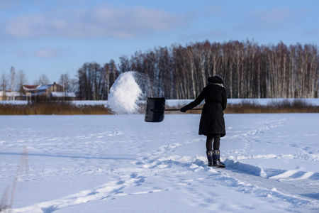 young woman in black coat cleaning ice from snow on a frozen lake to make skating ground. throwing snow in the airの写真素材