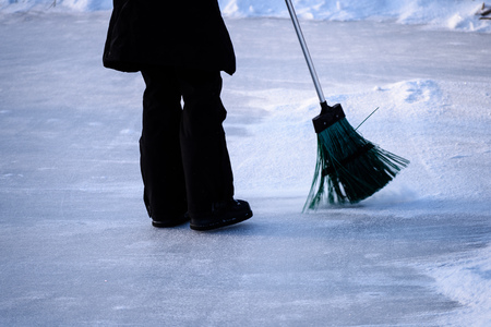 young woman in black coat cleaning ice from snow on a frozen lake to make skating groundの写真素材