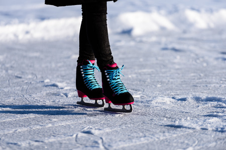 young woman in black coat skating on the frozen lake in snow with modern skates. close up shoot,...