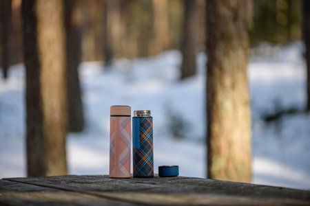 colorful thermoses on wooden table in winter forest with hot coffee. blur background copyspaceの写真素材