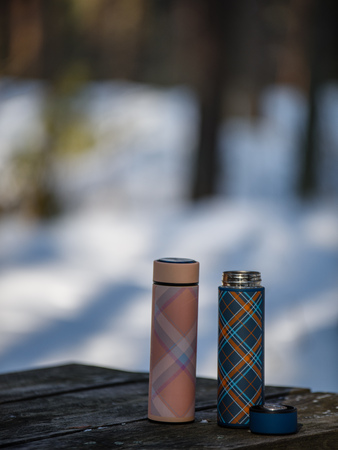 colorful thermoses on wooden table in winter forest with hot coffee. blur background copyspaceの写真素材