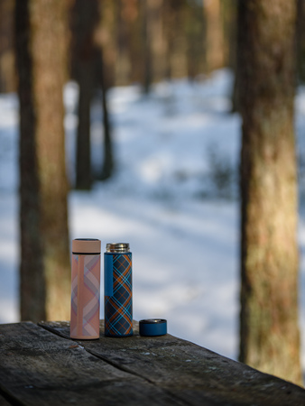 colorful thermoses on wooden table in winter forest with hot coffee. blur background copyspaceの写真素材