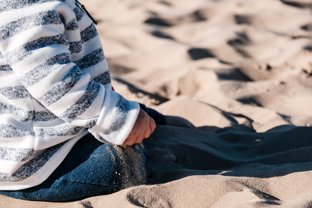 baby hand playing with sand on the beach with harsh sunlightの写真素材