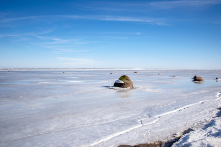 frozen lake shore in winter with footsteps in the snow and ice blocks across the scene. old treesの写真素材