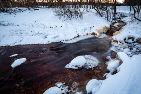 long exposure rocky mountain river in winter with high water stream level and white snowの写真素材