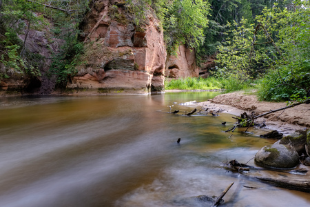 long exposure rocky mountain river in summer with high water stream level in forest with trees and sandy foreground shoreの写真素材