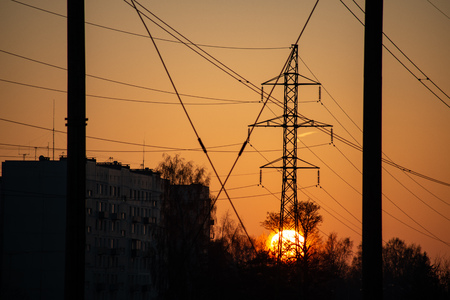red sunset with sun setting down behind large electricity power line metal poles. dark silhouettes of wiresの写真素材