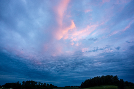 high contrast clouds on blue sky over natural landscape in summer at sunset timeの写真素材