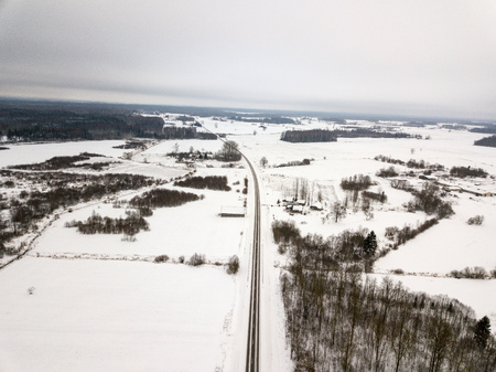 country asphalt roads in winter and small village from above. aerial drone image in cold winter snow white fields and forestsの写真素材