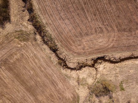 aerial view of small country river bed wavy in spring time in countryside with dry grass and some bushes. fields textureの写真素材