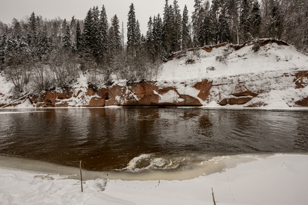 frozen forest river in winter with sandstone cliffsの写真素材
