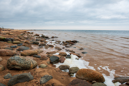 lonely empty sea beach with white sand, large rocks and old wooden trunks on the shore. spring landscapeの写真素材