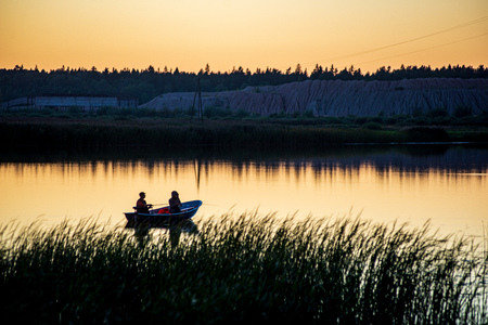 calm countryside lake river in sunset with fisherman in a boatの写真素材