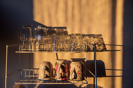 dishes and glasses on a dryer in kitchen in sunset light with shadows and reflectionsの写真素材