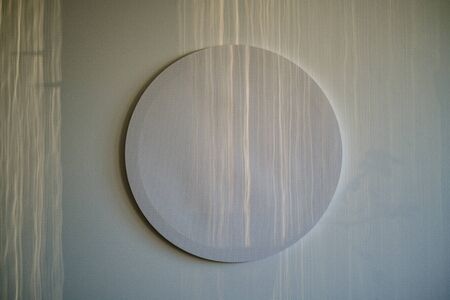 empty decorative round white canvas for painting on the white wall  with sun rays and shadowsの写真素材