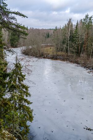 half frozen river in late autumn with trees with no leaves.  partial ice cover over river Gauja in Latviaの写真素材
