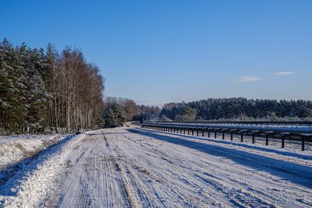 car tracks in the snow on the winter road in sunny day with frost on the treesの写真素材