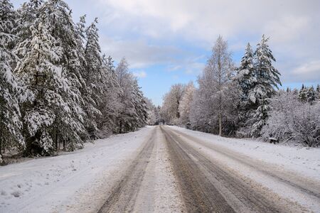 car tracks in the snow on the winter road in sunny day with frost on the treesの写真素材