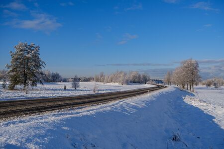 car tracks in the snow on the winter road in sunny day with frost on the treesの写真素材