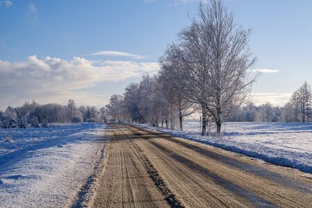 car tracks in the snow on the winter road in sunny day with frost on the treesの写真素材
