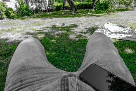 man legs with phone resting in parkの写真素材