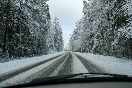 car tracks in the snow on the winter road in sunny day with frost on the treesの写真素材