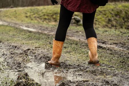 woman jumping in the puddle of mud in autumn with orange rubber bootsの写真素材