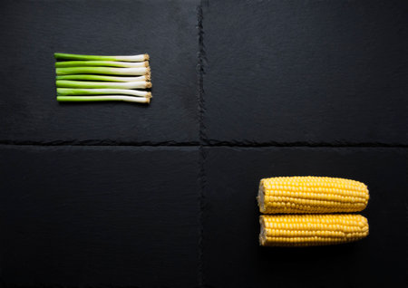 Two vegetables, corn, spring onions on slate platform