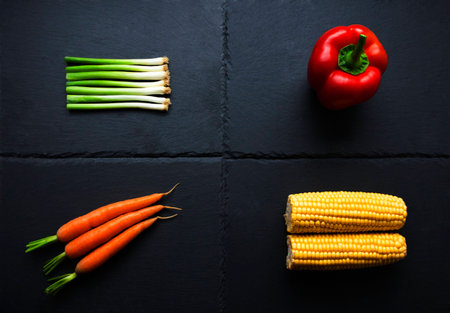 Four individual vegetables; onions, pepper, carrots, corn on the cob on slate plateの写真素材