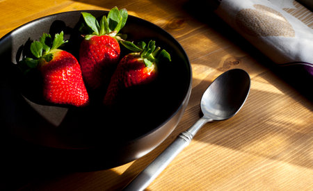 Several Strawberries in Black Bowl on Wooden Surfaceの写真素材