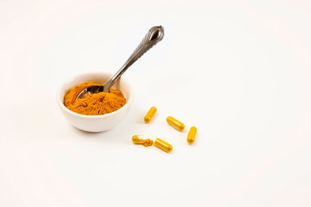 Turmeric powder in small dish with silver spoon. Turmeric capsules on white surface.の写真素材