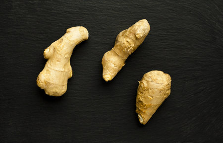 Three segments of organic ginger on black, slate surface