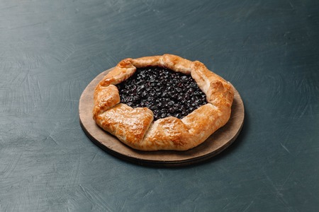 Galette with seasonal berries. Galette with black currant. Flat lay crispy summer berry pie on a gray-blue backgroundの写真素材