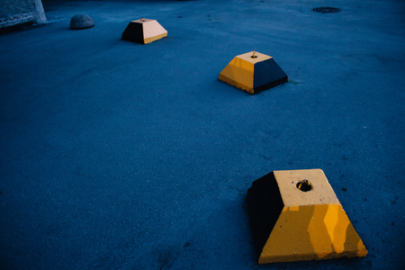 The concrete block of the truncated yellow pyramid against the background of blue asphalt prevents the movement of cars on the sidewalkの写真素材