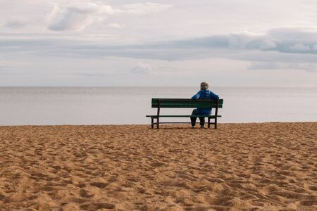 A woman sits alone on a bench. Attractive girl sitting on a wooden bench with a stunning view of the sea.の写真素材
