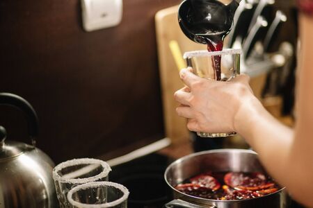 Girl pours hot mulled wine into glasses. The edges of the glasses are coated with sugar. The frame contains female hands a pan with mulled wine and spicesの写真素材