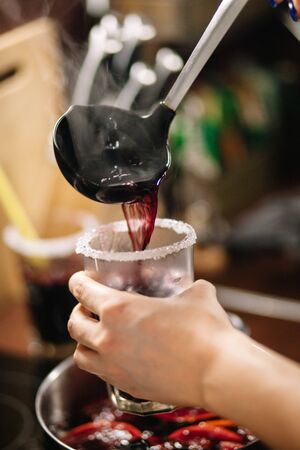 Girl pours hot mulled wine into glasses. The edges of the glasses are coated with sugar. The frame...