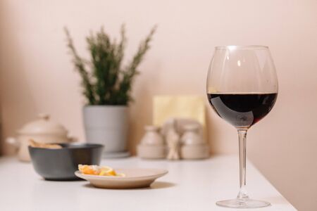 Glass of red wine on the kitchen table on a background of a plate with tangerines and a pot with a houseplantの写真素材