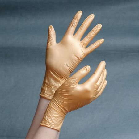 Hands in nitrile gloves of gold color on a gray background with a gradient. Square aspect ratioの写真素材