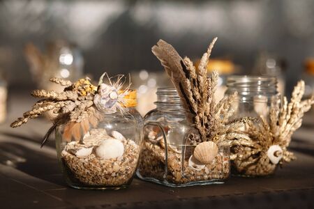 The glass jar is decorated with feathers, ears of grass and shells. Decoration on the wedding table....